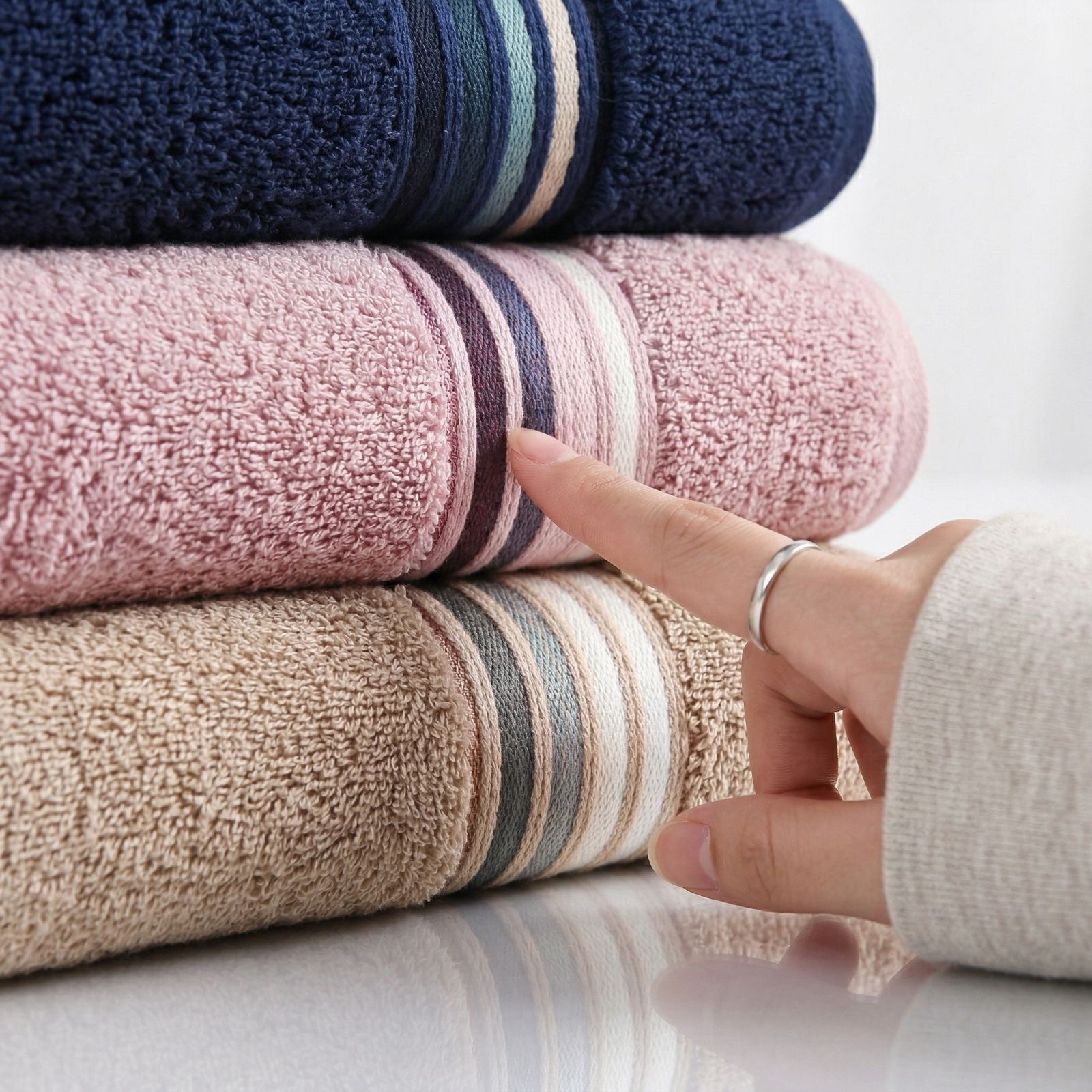 A hand resting on a stack of folded House of Linen towels.